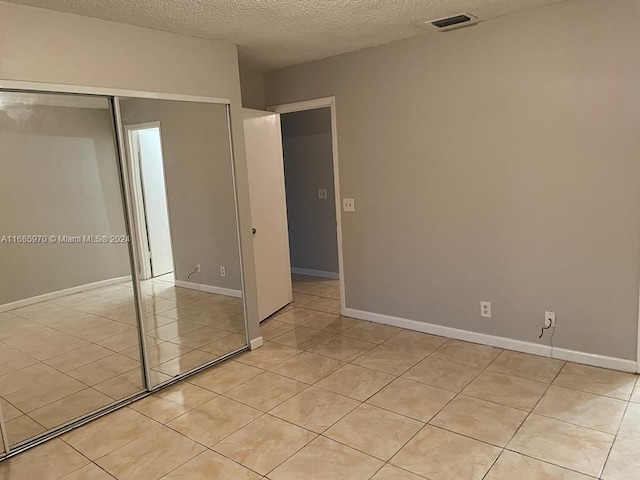 unfurnished bedroom with a closet, a textured ceiling, and light tile patterned floors