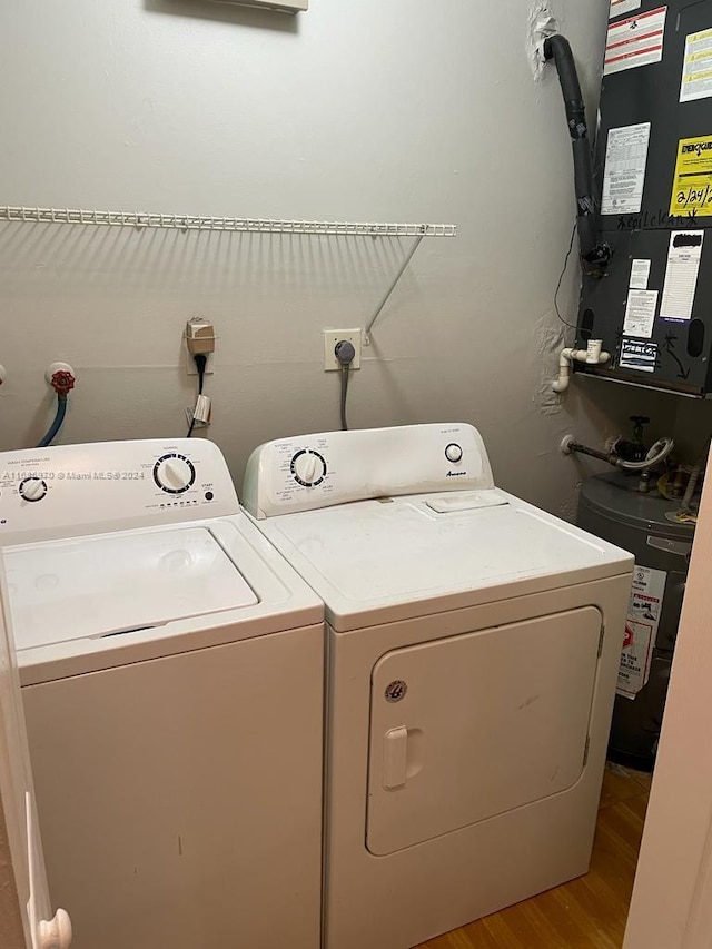 laundry area with water heater, washer and clothes dryer, and light wood-type flooring