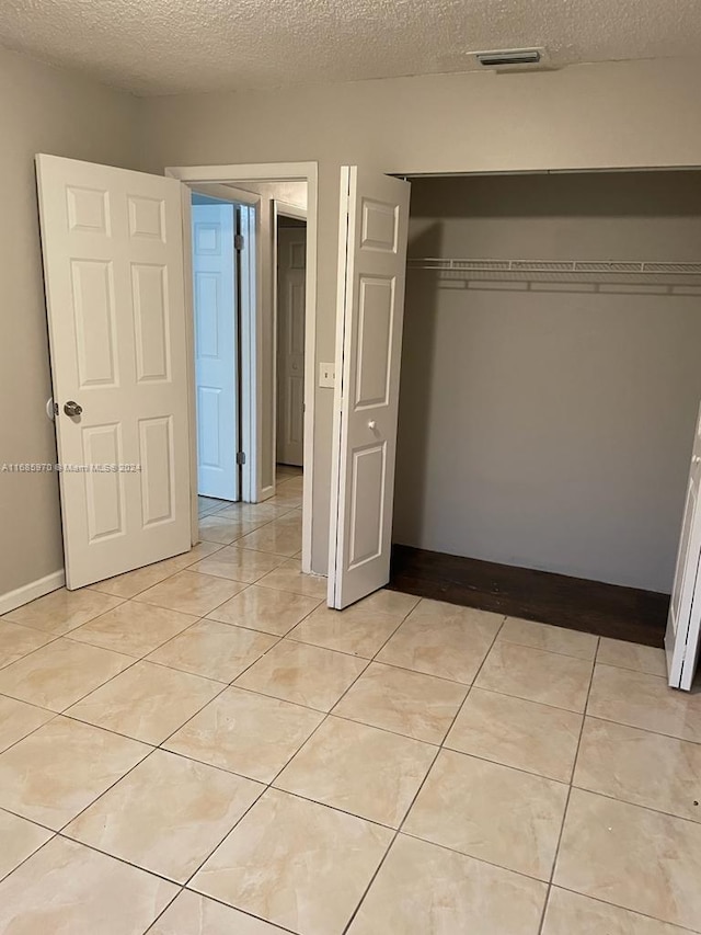 unfurnished bedroom featuring a closet, a textured ceiling, and light tile patterned floors