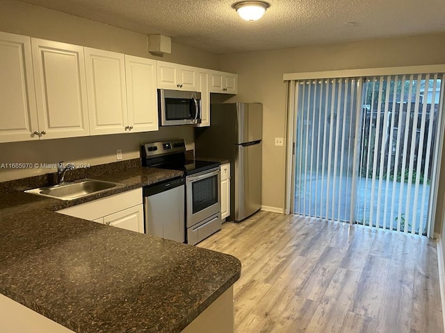 kitchen featuring sink, white cabinets, appliances with stainless steel finishes, a textured ceiling, and light hardwood / wood-style floors