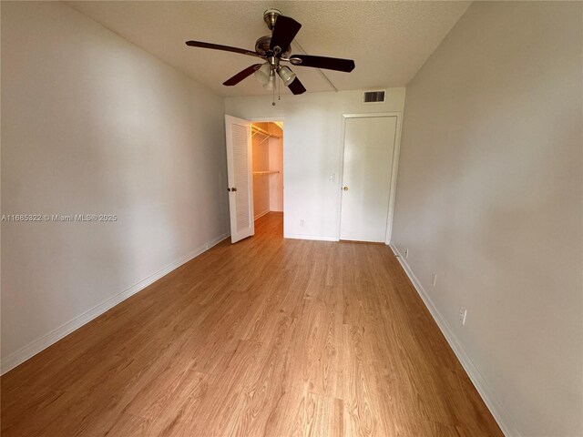 empty room with a textured ceiling, light wood-type flooring, and ceiling fan