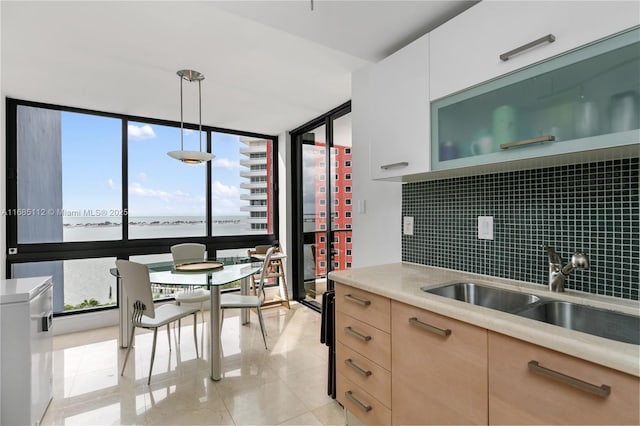 kitchen featuring pendant lighting, sink, a water view, white cabinets, and light brown cabinetry