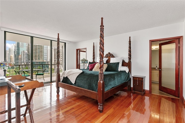 bedroom with hardwood / wood-style floors, a wall of windows, access to outside, and a textured ceiling