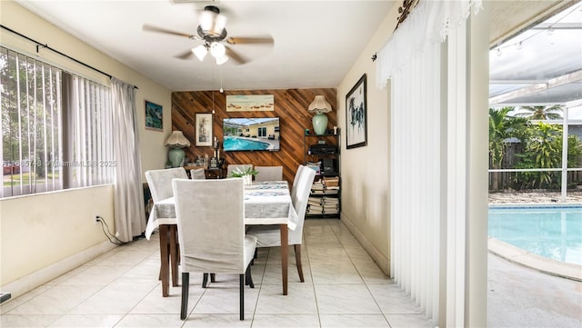 dining space featuring wooden walls, ceiling fan, and light tile patterned flooring