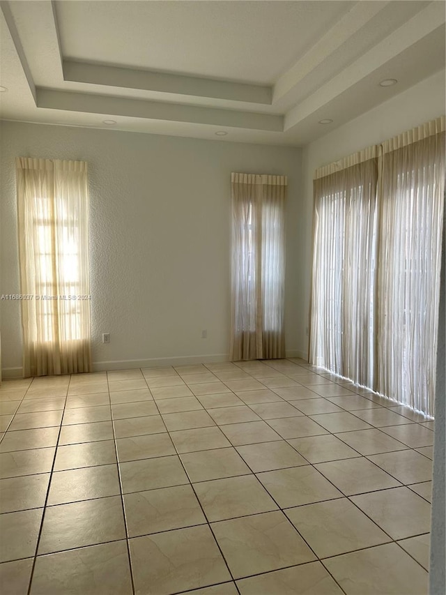 tiled empty room featuring a raised ceiling