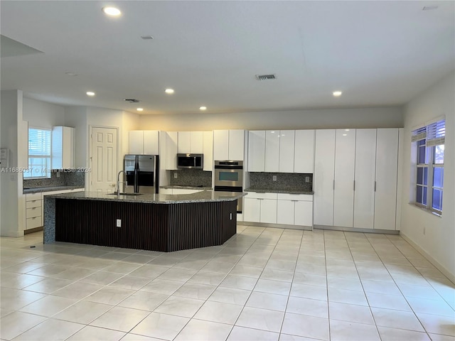 kitchen featuring a kitchen island with sink, sink, dark stone countertops, appliances with stainless steel finishes, and white cabinetry