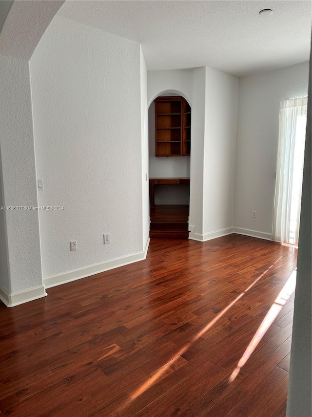 empty room with built in shelves, a textured ceiling, and dark wood-type flooring