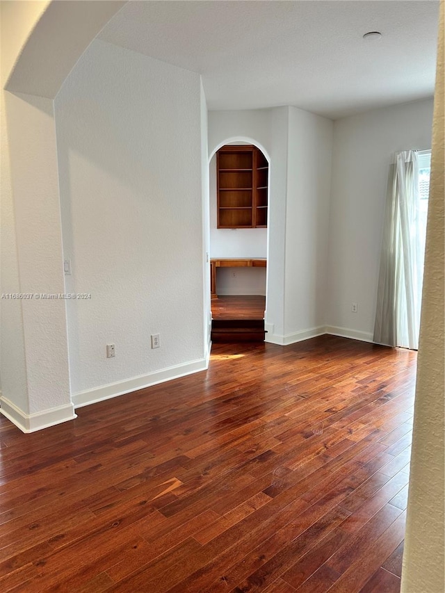 empty room featuring built in shelves and dark hardwood / wood-style floors