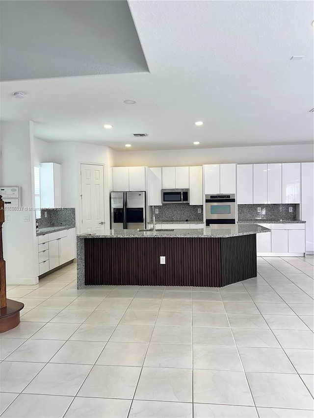 kitchen featuring light tile patterned floors, appliances with stainless steel finishes, tasteful backsplash, a large island, and white cabinetry