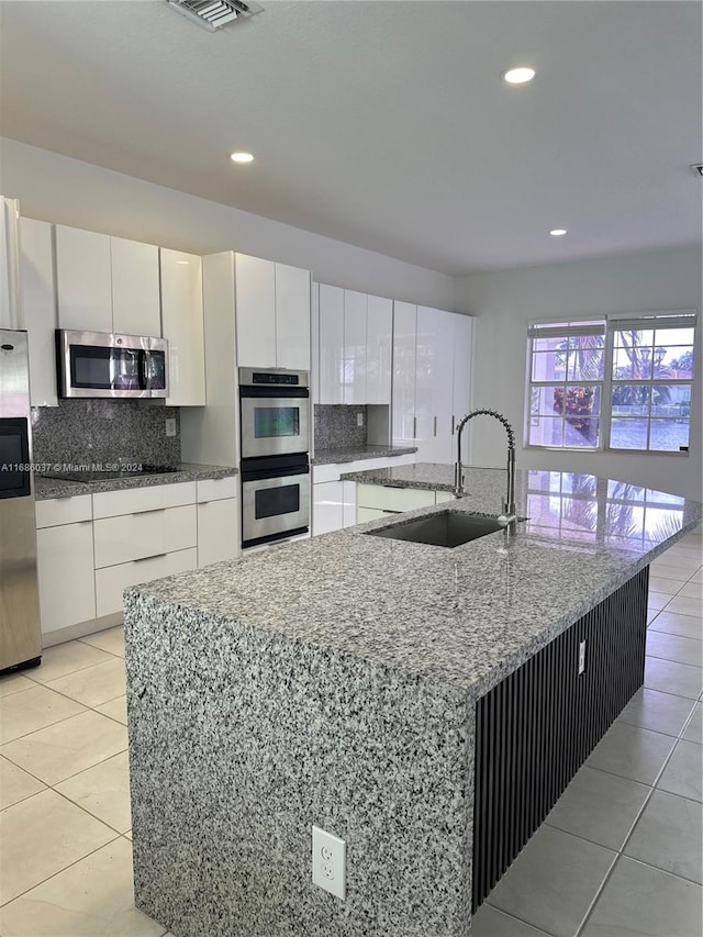 kitchen with stainless steel appliances, sink, white cabinetry, a large island, and light tile patterned flooring