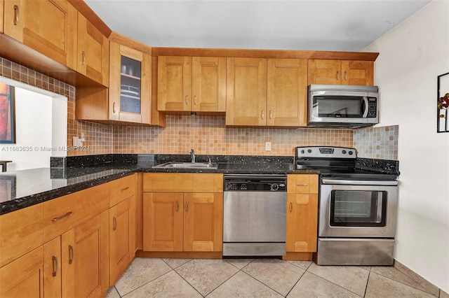 kitchen featuring backsplash, dark stone counters, sink, light tile patterned flooring, and appliances with stainless steel finishes