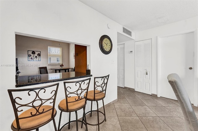 kitchen featuring a textured ceiling, light tile patterned floors, kitchen peninsula, and a kitchen breakfast bar