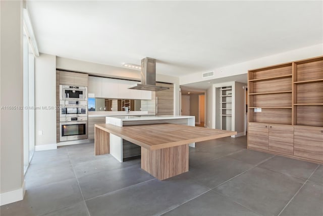 kitchen with white cabinets, double oven, island range hood, and a kitchen island