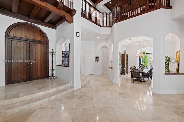 foyer featuring beamed ceiling, a towering ceiling, a notable chandelier, and wood ceiling