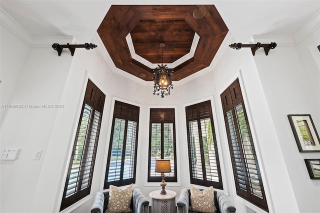 living area featuring a raised ceiling, a wealth of natural light, ornamental molding, and a notable chandelier