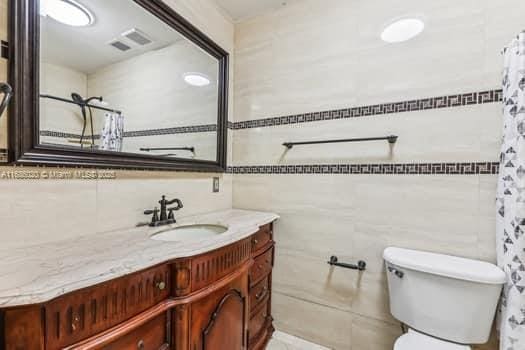 bathroom featuring toilet, tile walls, and vanity