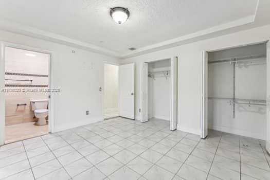 unfurnished bedroom featuring two closets, ensuite bathroom, and a raised ceiling