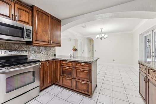 kitchen featuring light stone countertops, stainless steel appliances, backsplash, kitchen peninsula, and a notable chandelier