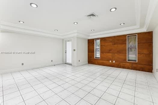 empty room with a raised ceiling, light tile patterned floors, and ornamental molding