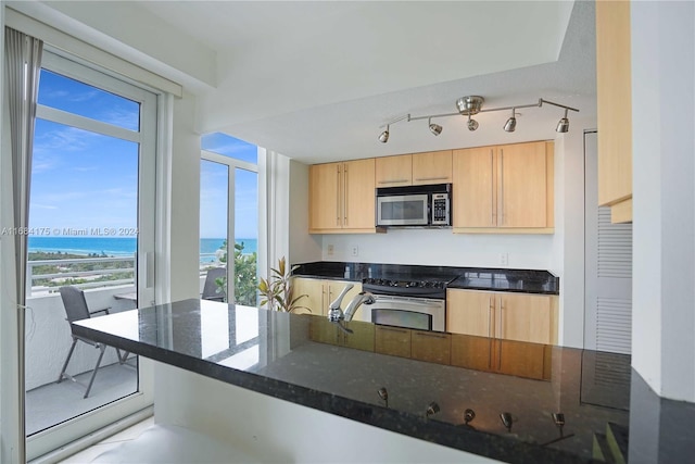 kitchen featuring light brown cabinetry, appliances with stainless steel finishes, plenty of natural light, dark stone counters, and a water view