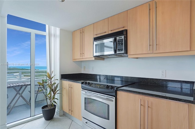 kitchen with light brown cabinetry, appliances with stainless steel finishes, dark stone counters, and light tile patterned floors