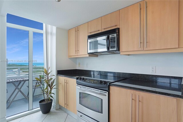 kitchen featuring appliances with stainless steel finishes, sink, light brown cabinetry, dark stone counters, and light tile patterned floors