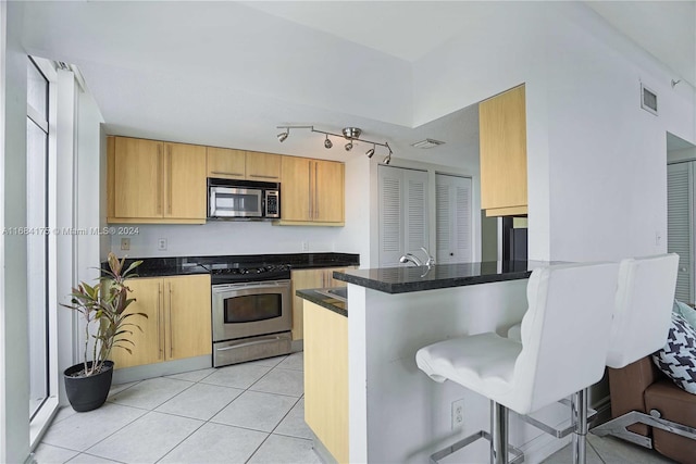 kitchen with appliances with stainless steel finishes, light tile patterned flooring, kitchen peninsula, and a kitchen bar