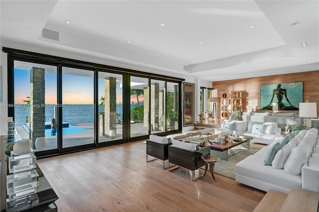 living room with a tray ceiling, french doors, a water view, and light hardwood / wood-style floors