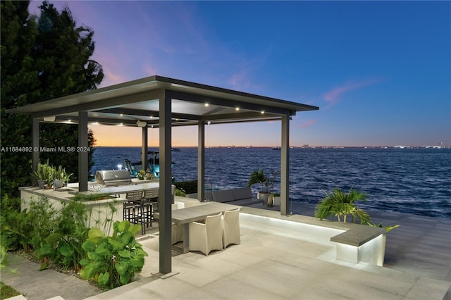 patio terrace at dusk featuring a water view, area for grilling, an outdoor hangout area, and a grill