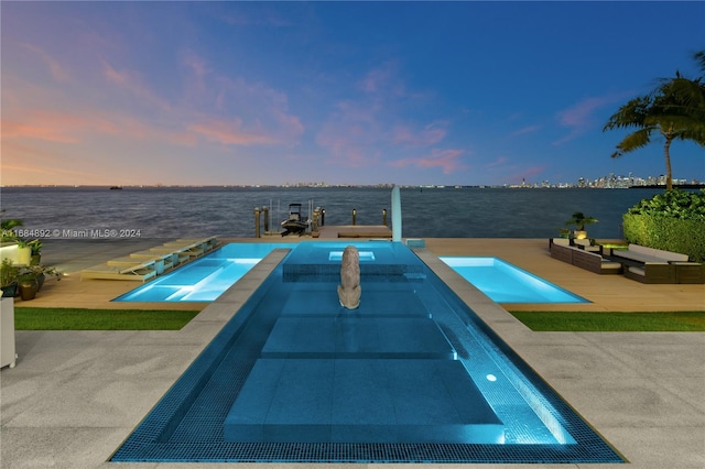 pool at dusk featuring a patio, an in ground hot tub, and a water view