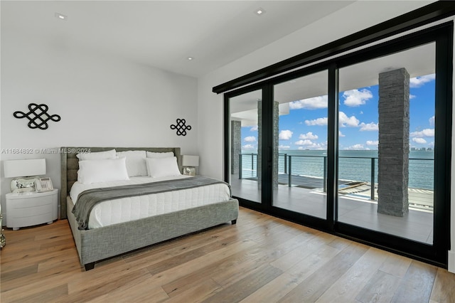 bedroom featuring a water view, light hardwood / wood-style floors, access to outside, and a wall of windows