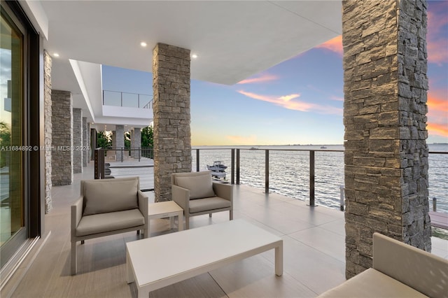 patio terrace at dusk featuring a water view, a balcony, and outdoor lounge area