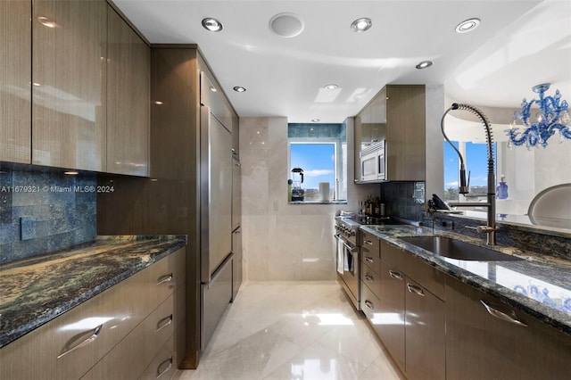 kitchen with dark stone countertops, backsplash, premium appliances, and sink