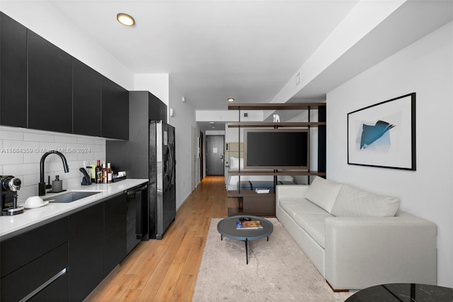 kitchen with sink, black appliances, light hardwood / wood-style flooring, and decorative backsplash