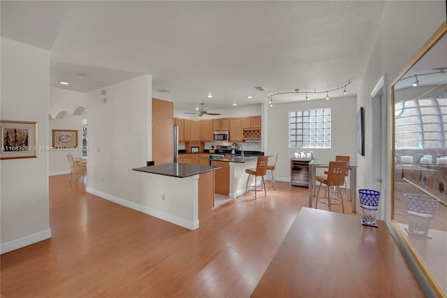 kitchen with track lighting, appliances with stainless steel finishes, a kitchen breakfast bar, a center island, and light wood-type flooring