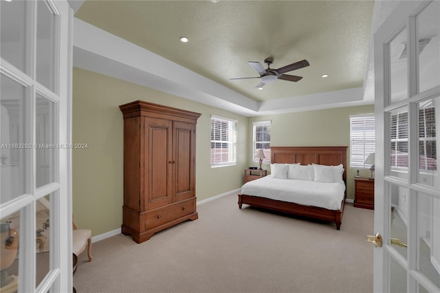 bedroom featuring ceiling fan, a textured ceiling, a raised ceiling, light colored carpet, and french doors