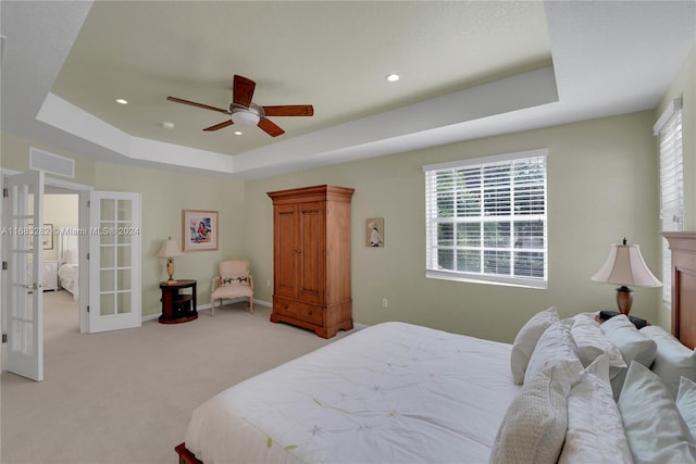 bedroom featuring a tray ceiling, french doors, light colored carpet, and ceiling fan