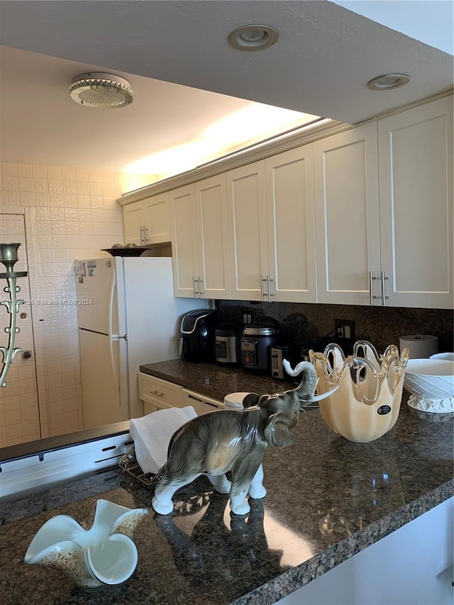 kitchen featuring white fridge, white cabinetry, tasteful backsplash, and dark stone counters