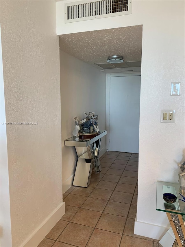 hallway with a textured ceiling and tile patterned flooring