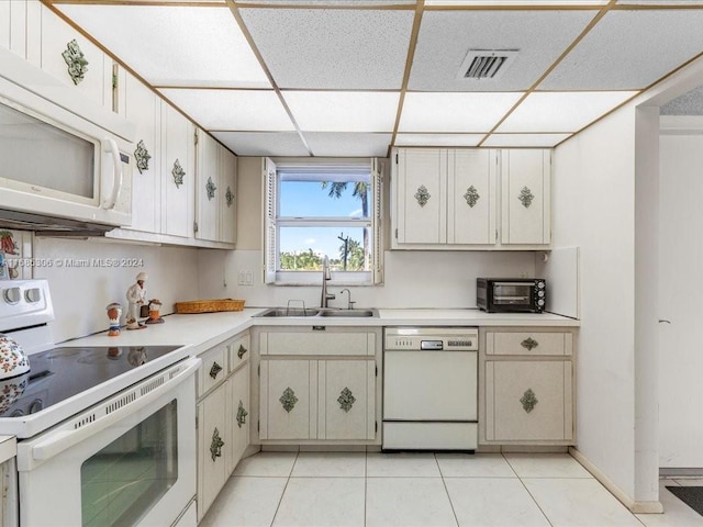 kitchen featuring sink, a drop ceiling, light tile patterned floors, white appliances, and white cabinets