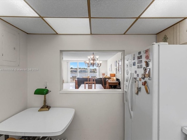 kitchen featuring electric panel, white fridge with ice dispenser, a drop ceiling, and an inviting chandelier