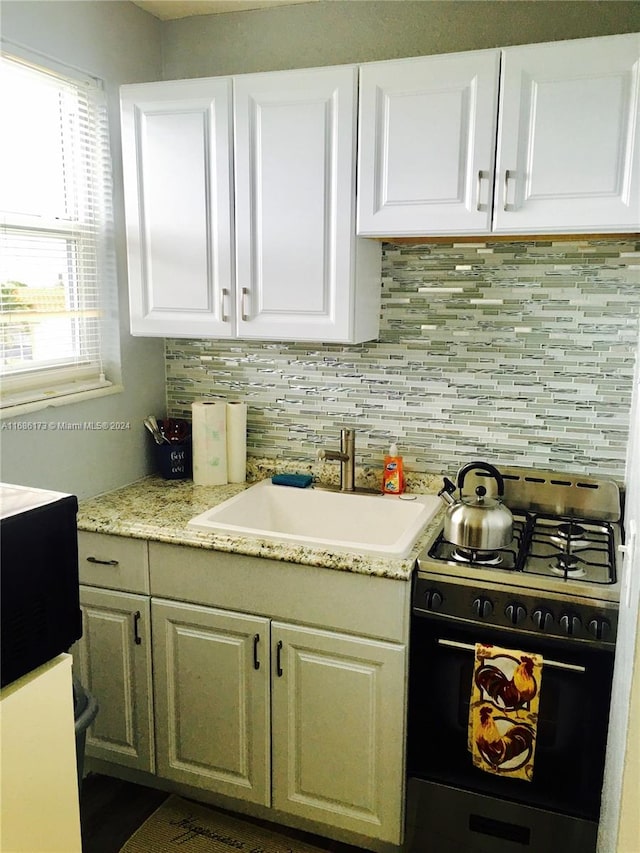 kitchen with stainless steel gas range oven, white cabinets, sink, and backsplash