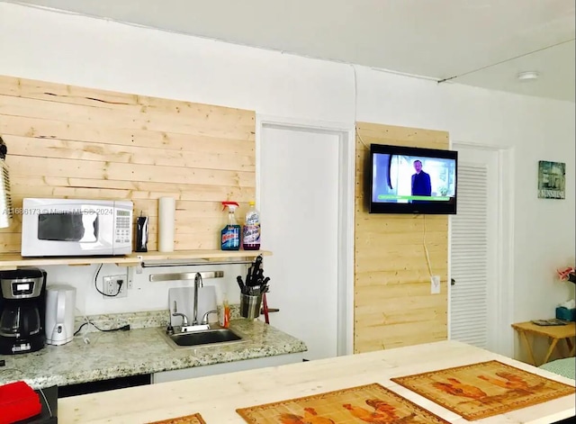 kitchen with sink, light stone counters, and wood walls