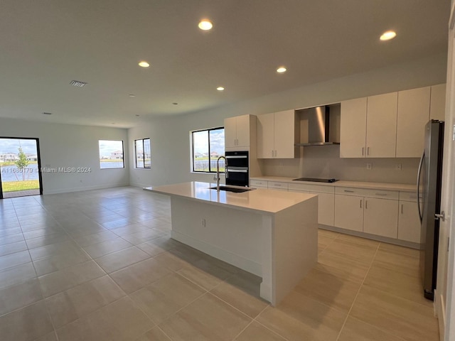 kitchen featuring a kitchen island with sink, sink, wall chimney exhaust hood, appliances with stainless steel finishes, and white cabinetry