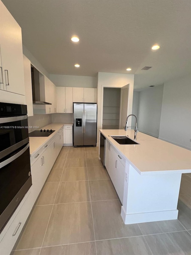 kitchen featuring appliances with stainless steel finishes, wall chimney range hood, sink, white cabinets, and a kitchen island