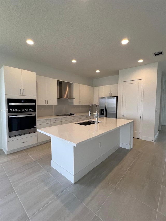 kitchen with white cabinetry, sink, wall chimney exhaust hood, stainless steel appliances, and a kitchen island with sink