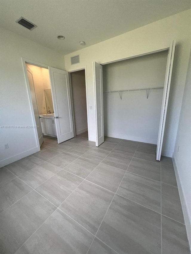 unfurnished bedroom featuring light tile patterned floors, ensuite bathroom, and a closet