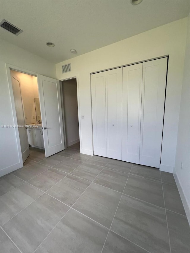 unfurnished bedroom with connected bathroom, a closet, and light tile patterned flooring