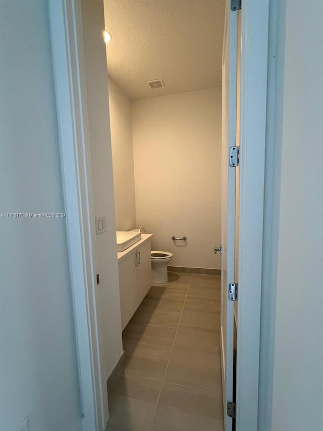 bathroom with tile patterned flooring, vanity, toilet, and a textured ceiling