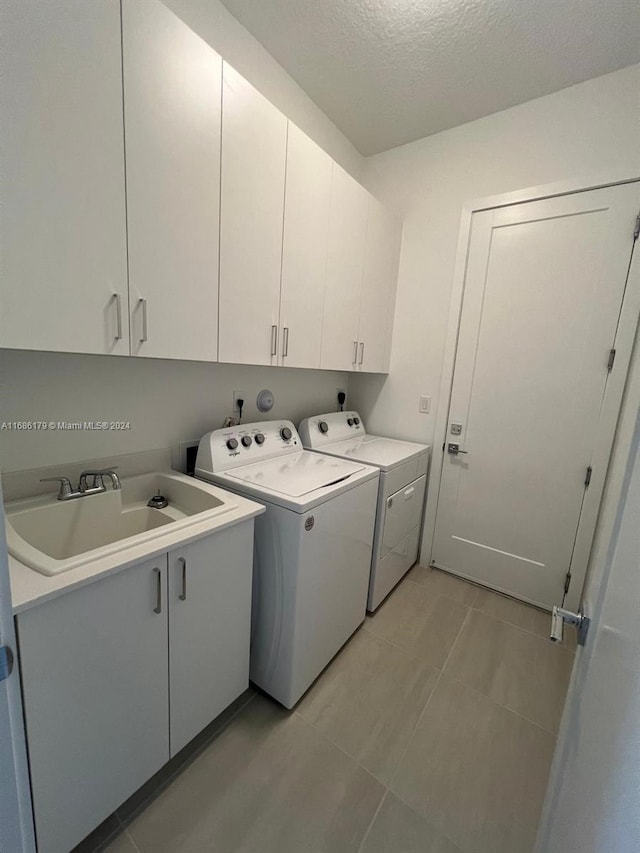 washroom featuring sink, cabinets, separate washer and dryer, a textured ceiling, and light tile patterned floors